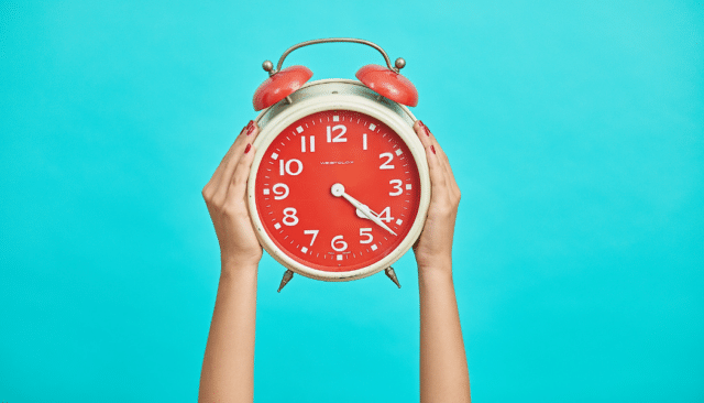 person holding up red old-school clock on blue background