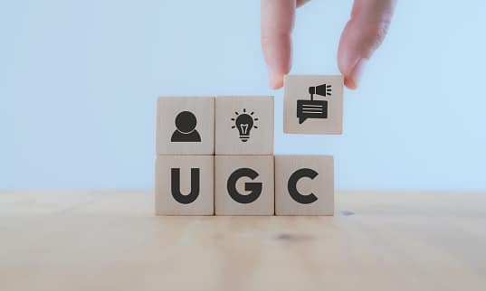 Black Friday 2021 - User-generated content concept.(UGC) Online marketing concept. Customer create content on social media . Close up hand put wooden cube with "UGC"icon and abbreviation on white background,copy space