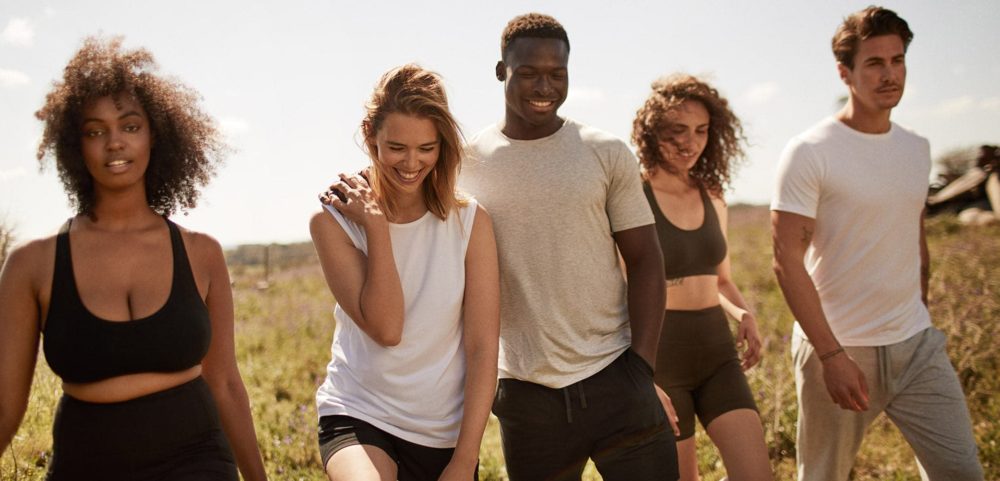 group of five 20-somethings walking through a field smiling in casual and athletic wear
