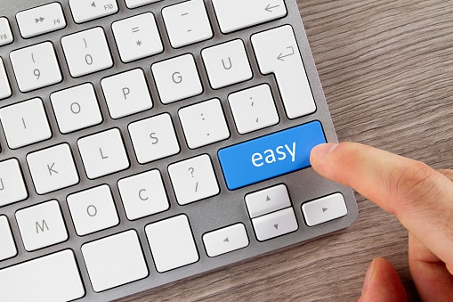 Concept shot with computer keyboard. This is a close-up shot of human finger while it pushes the blue easy button on gray computer keyboard on office desk..