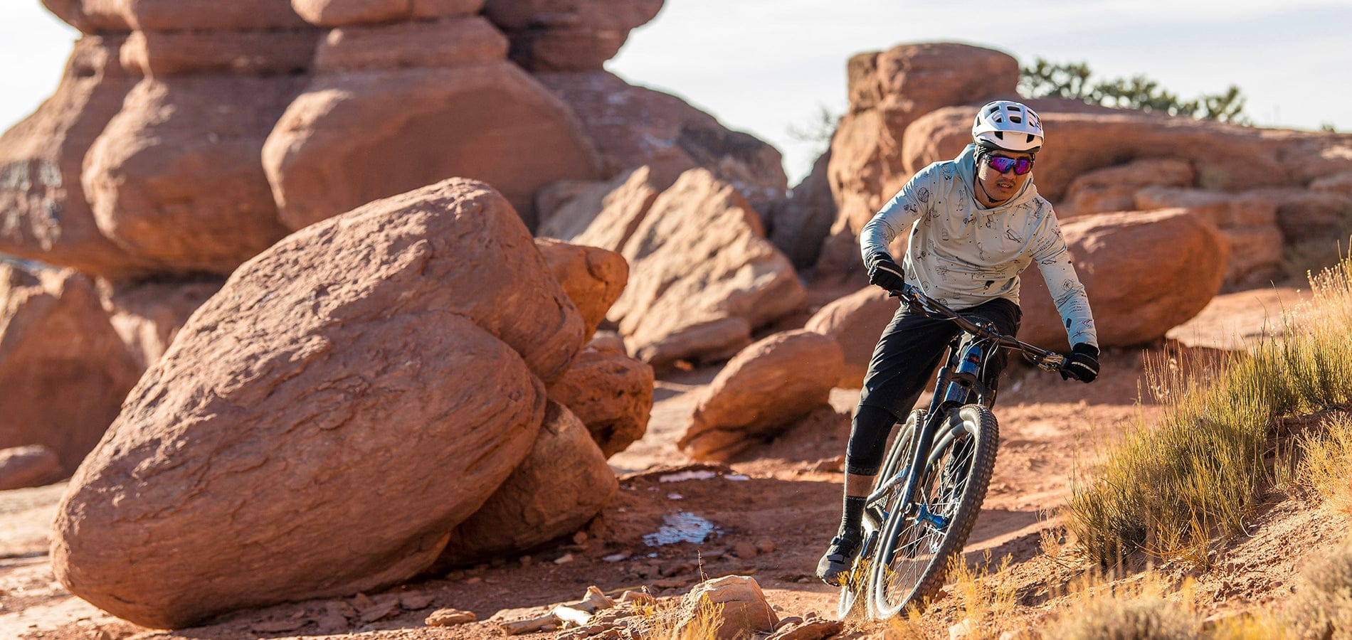 Man riding bike with helmet and on. Riding next to red rocks in a desert setting
