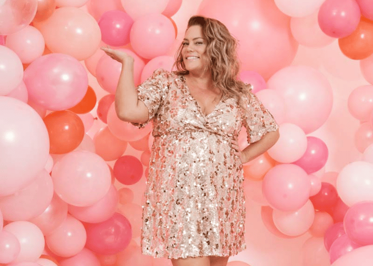 woman smiling in pink sequin mini dress with pink balloon wall behind her