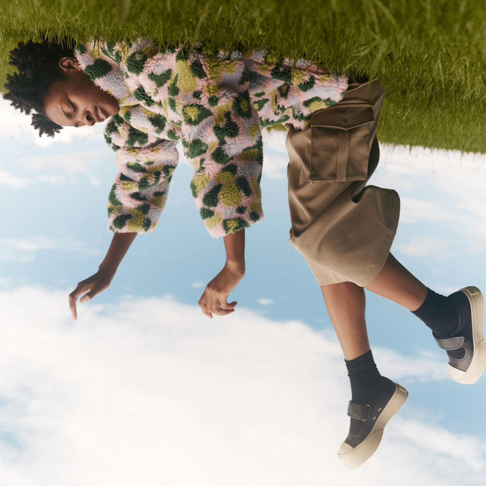 upside down image of a person laying on grass in tan pants and colorful shirt, and sneakers. Legs in the air.
