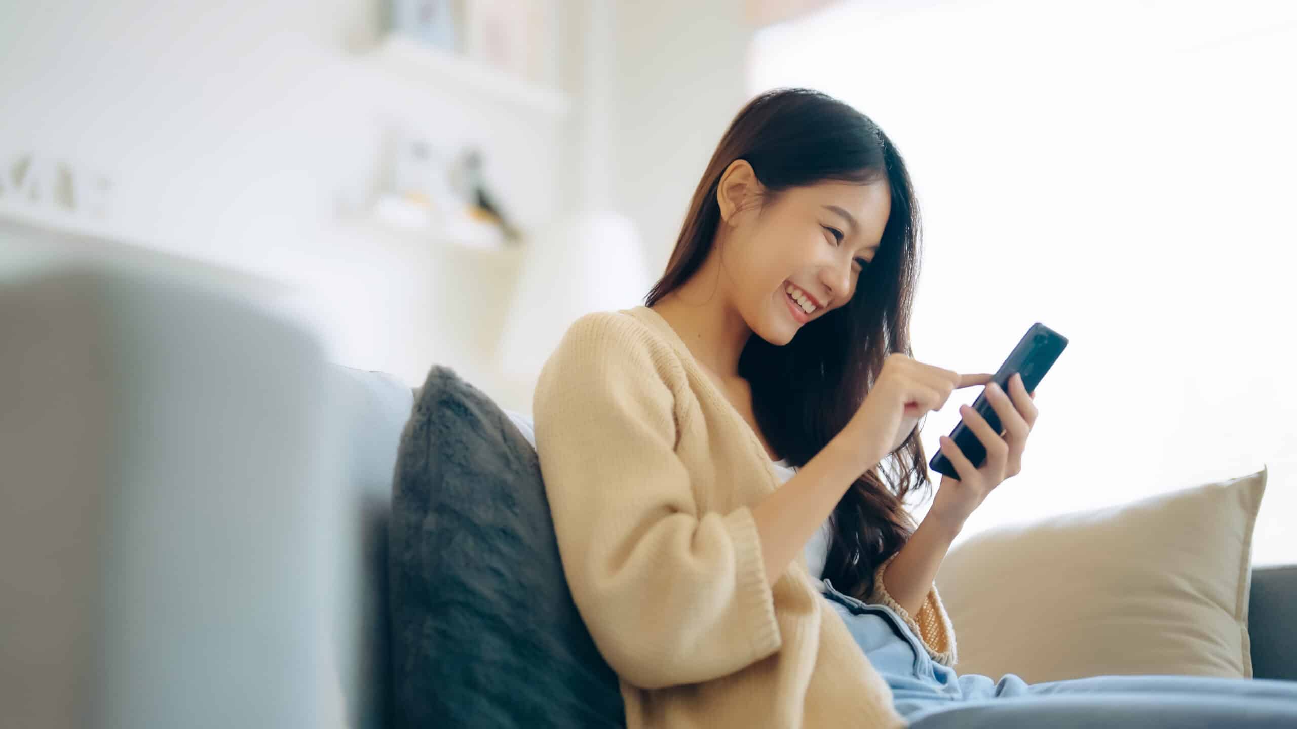 Happy woman relax on comfortable couch at home on smartphone