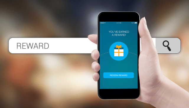 person holding up phone with a search bar in background. the words "rewards achieved" on the screen